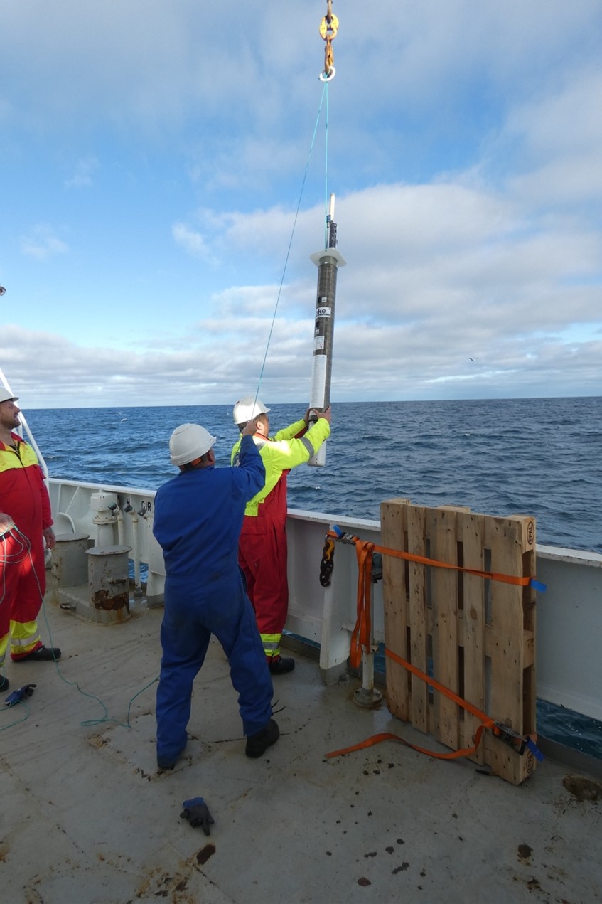 Three persons on deck, deploying equipment off the vessel side.